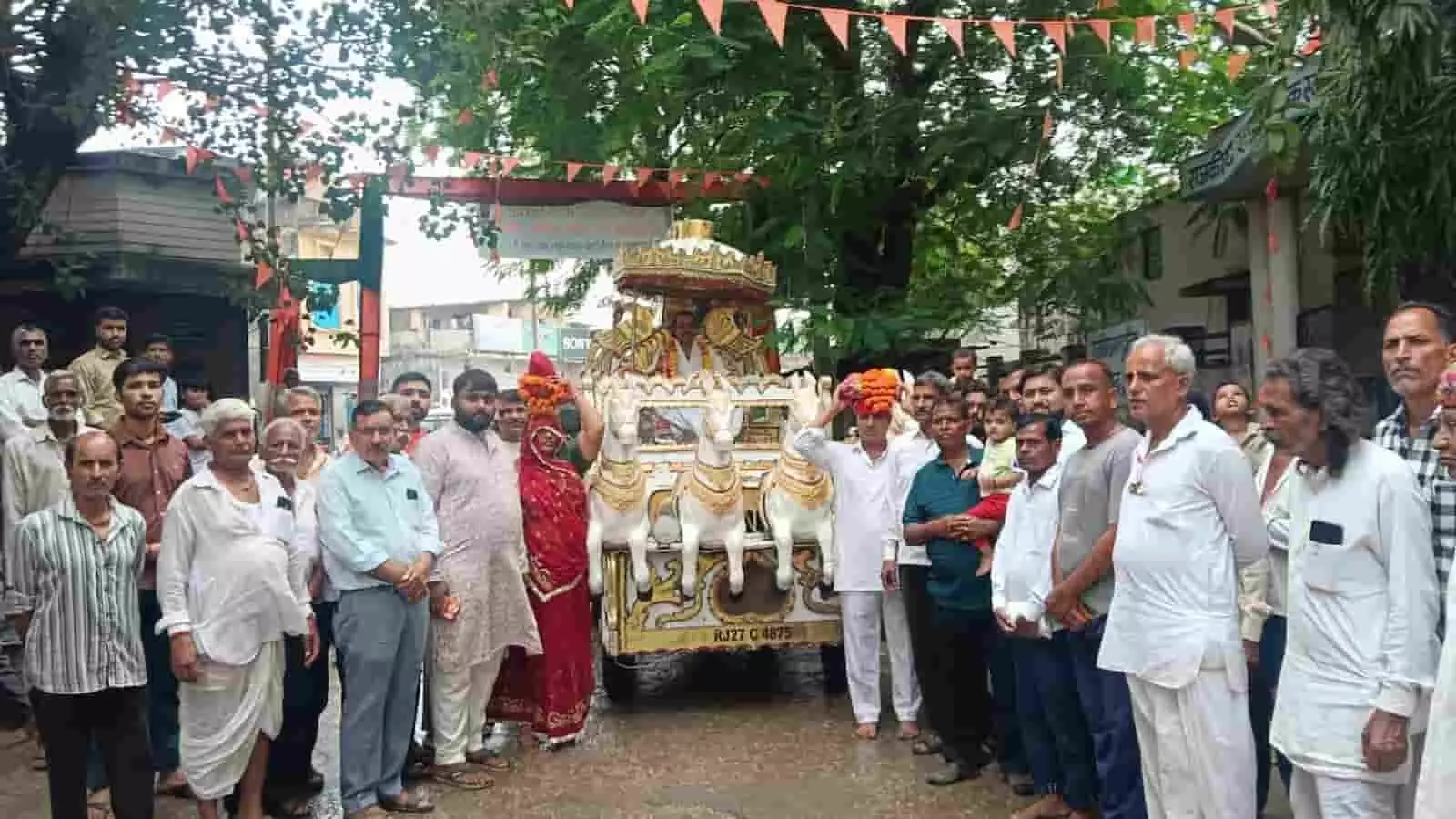 खेरोदा की सड़क पर सजे हुए रथ के साथ खड़े पुरुष और महिलाएं शोभायात्रा के दौरान एकत्रित हैं। खेरोदा की सड़क पर सजे हुए रथ के साथ खड़े पुरुष और महिलाएं शोभायात्रा के दौरान एकत्रित हैं।