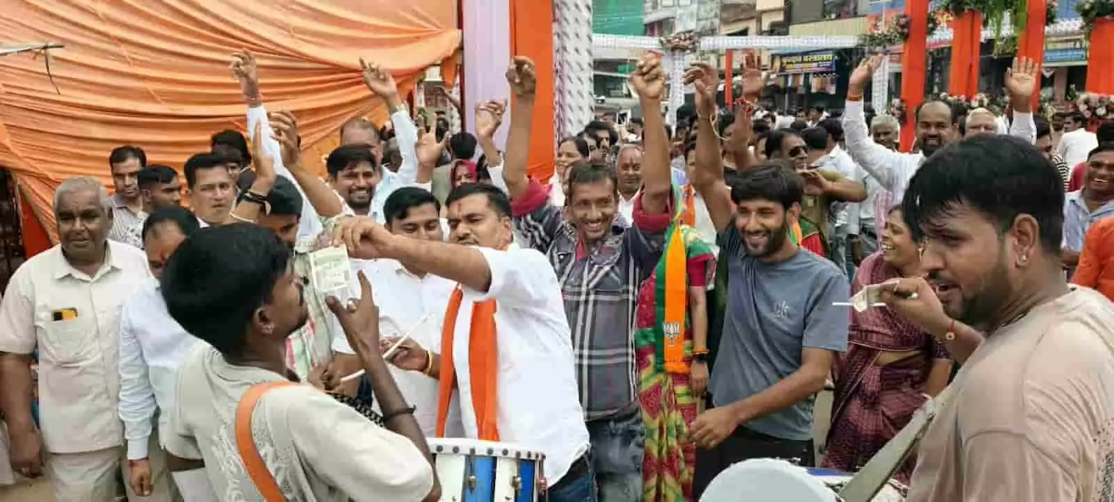 तस्वीर में भगवा दुपट्टा पहने पुरुष और महिलाएं ढोल बजाते व्यक्ति के पास हाथ उठाकर जश्न मनाती दिख रही हैं। तस्वीर में भगवा दुपट्टा पहने पुरुष और महिलाएं ढोल बजाते व्यक्ति के पास हाथ उठाकर जश्न मनाती दिख रही हैं।