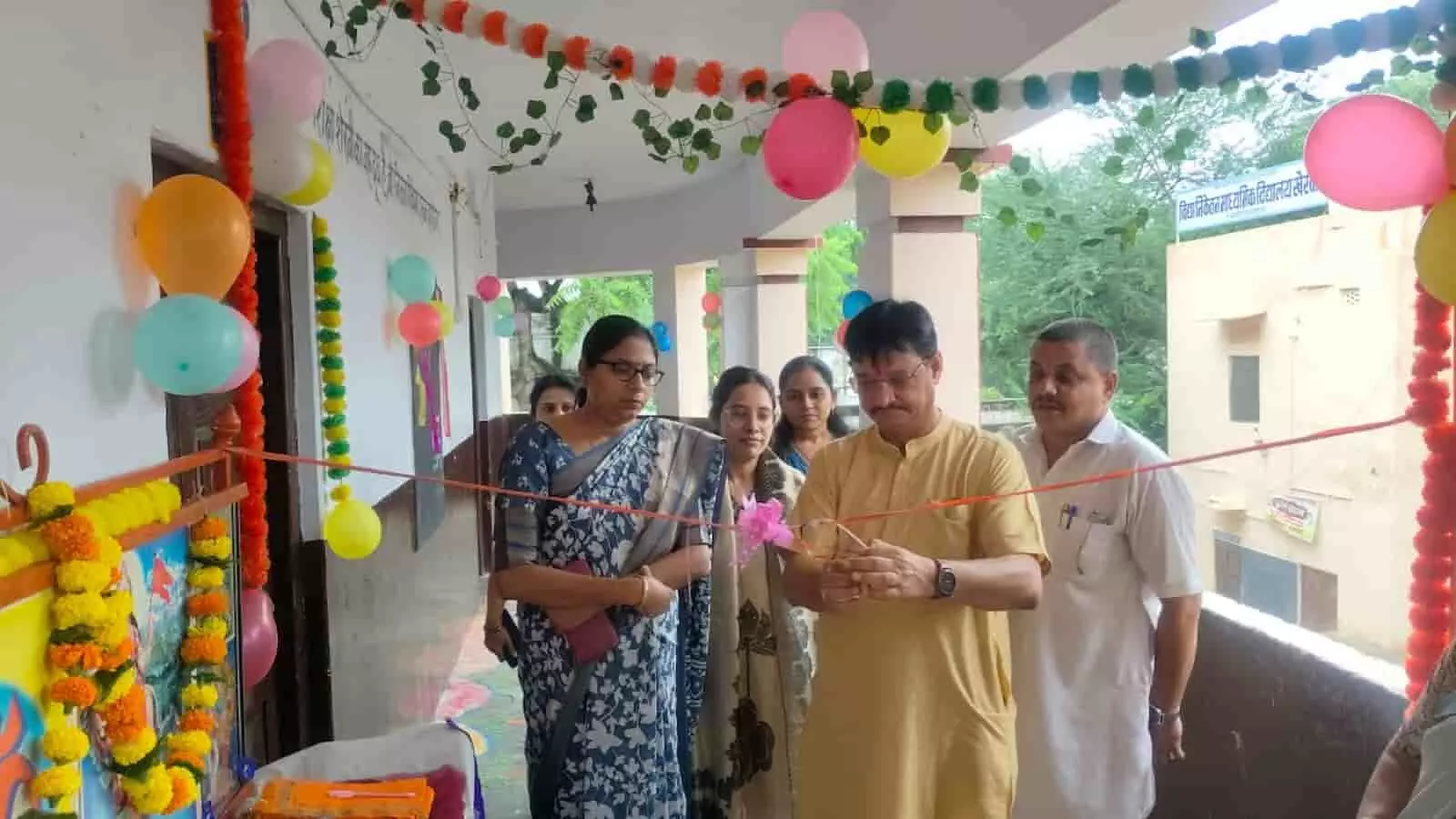 तस्वीर में बाएं से दाएं महिलाएं और पुरुष अतिथि सजाए गए विद्यालय परिसर में रिबन काट रहे हैं। तस्वीर में बाएं से दाएं महिलाएं और पुरुष अतिथि सजाए गए विद्यालय परिसर में रिबन काट रहे हैं।