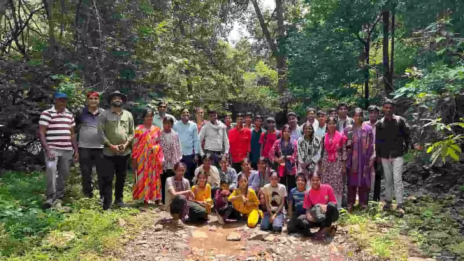 तस्वीर में घने जंगल के कच्चे रास्ते पर खड़े और बैठे प्रतिभागियों का समूह दिखाई दे रहा है। तस्वीर में घने जंगल के कच्चे रास्ते पर खड़े और बैठे प्रतिभागियों का समूह दिखाई दे रहा है।
