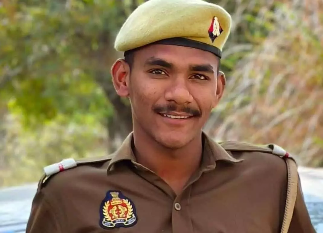 तस्वीर में एक युवा पुलिसकर्मी खाकी वर्दी और कैप पहने हुए कैमरे की ओर देखकर मुस्कुरा रहे हैं। तस्वीर में एक युवा पुलिसकर्मी खाकी वर्दी और कैप पहने हुए कैमरे की ओर देखकर मुस्कुरा रहे हैं।