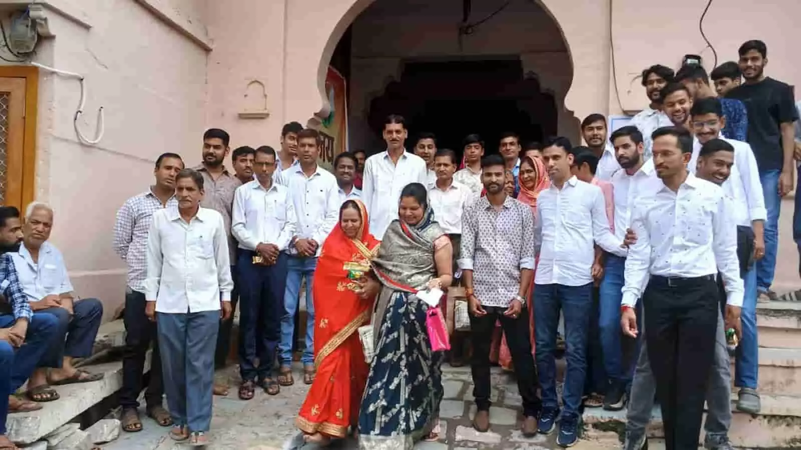 तस्वीर में दिख रही भवन की सीढ़ियों और प्रवेश द्वार के पास लोग एक साथ खड़े हैं। तस्वीर में दिख रही भवन की सीढ़ियों और प्रवेश द्वार के पास लोग एक साथ खड़े हैं।