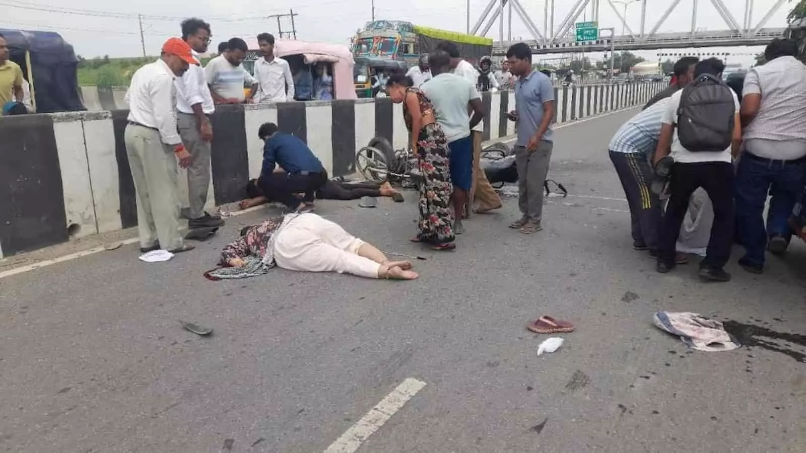 तस्वीर में बाएं से दाएं खड़े लोगों, सड़क पर लेटे हुए व्यक्तियों और क्षतिग्रस्त मोटरसाइकिलों के पास भीड़ दिखाई दे रही है। तस्वीर में बाएं से दाएं खड़े लोगों, सड़क पर लेटे हुए व्यक्तियों और क्षतिग्रस्त मोटरसाइकिलों के पास भीड़ दिखाई दे रही है।