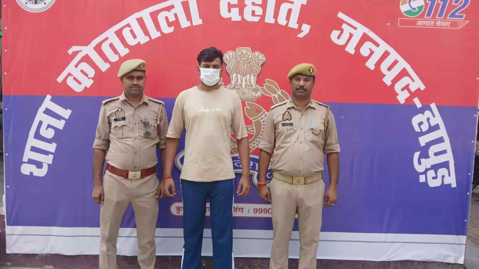 तस्वीर में बाएं और दाएं खाकी वर्दी पहने दो पुलिसकर्मी खड़े हैं, और उनके बीच केंद्र में मास्क लगाए एक व्यक्ति खड़ा है। तस्वीर में बाएं और दाएं खाकी वर्दी पहने दो पुलिसकर्मी खड़े हैं, और उनके बीच केंद्र में मास्क लगाए एक व्यक्ति खड़ा है।