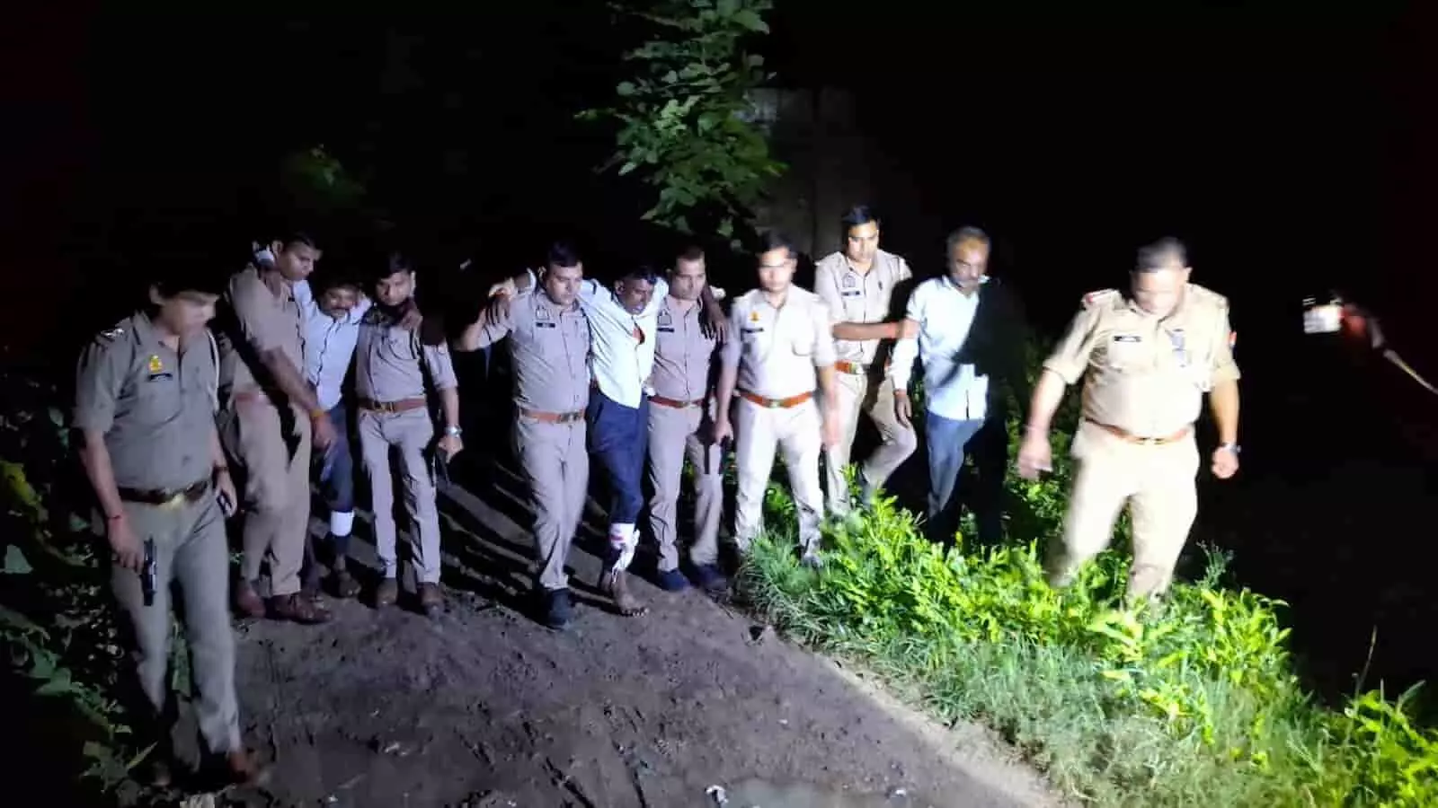 तस्वीर में खाकी वर्दी पहने कई पुलिसकर्मियों के साथ कुछ व्यक्ति अंधेरे में रास्ते पर चलते दिखाई दे रहे हैं। तस्वीर में खाकी वर्दी पहने कई पुलिसकर्मियों के साथ कुछ व्यक्ति अंधेरे में रास्ते पर चलते दिखाई दे रहे हैं।