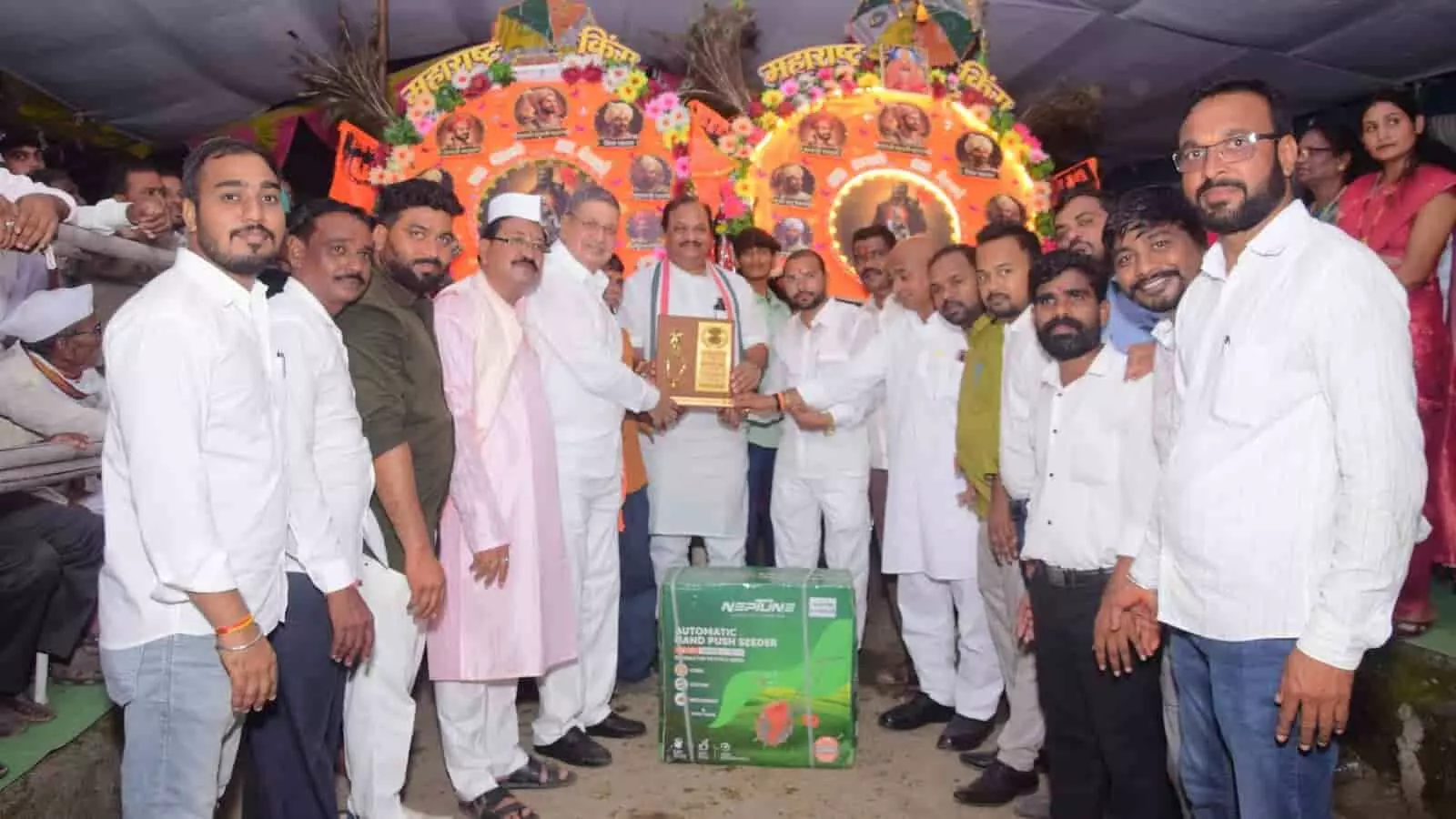 तस्वीर में दिख रही समिति के लोग मंच पर कृषि उपकरण के साथ व्यक्ति को स्मृति चिन्ह भेंट कर रहे हैं।