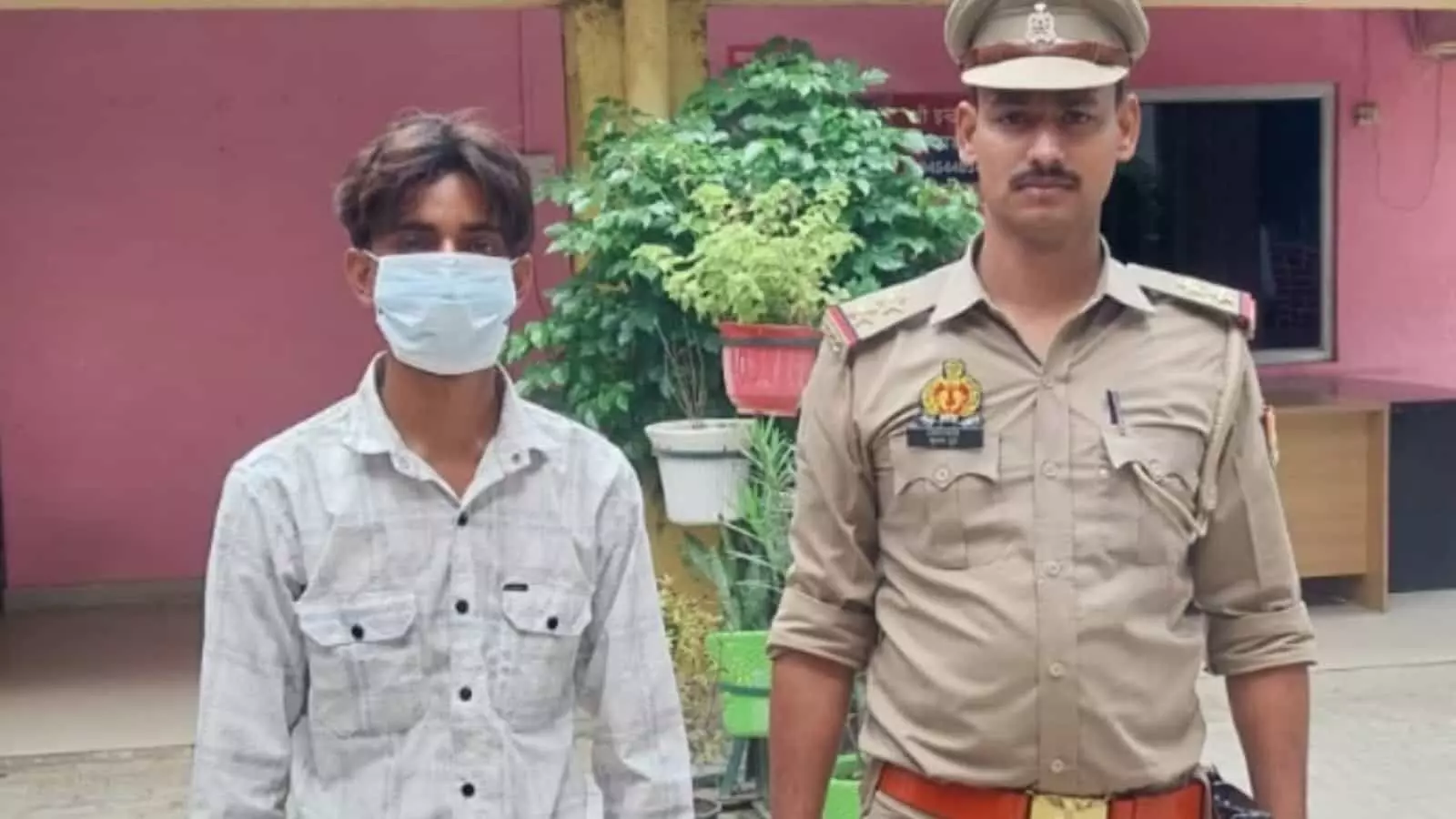 तस्वीर में बाएं तरफ मास्क पहने एक युवक खड़ा है और उसके दाहिने ओर खाकी वर्दी पहने पुलिसकर्मी खड़े हैं। तस्वीर में बाएं तरफ मास्क पहने एक युवक खड़ा है और उसके दाहिने ओर खाकी वर्दी पहने पुलिसकर्मी खड़े हैं।