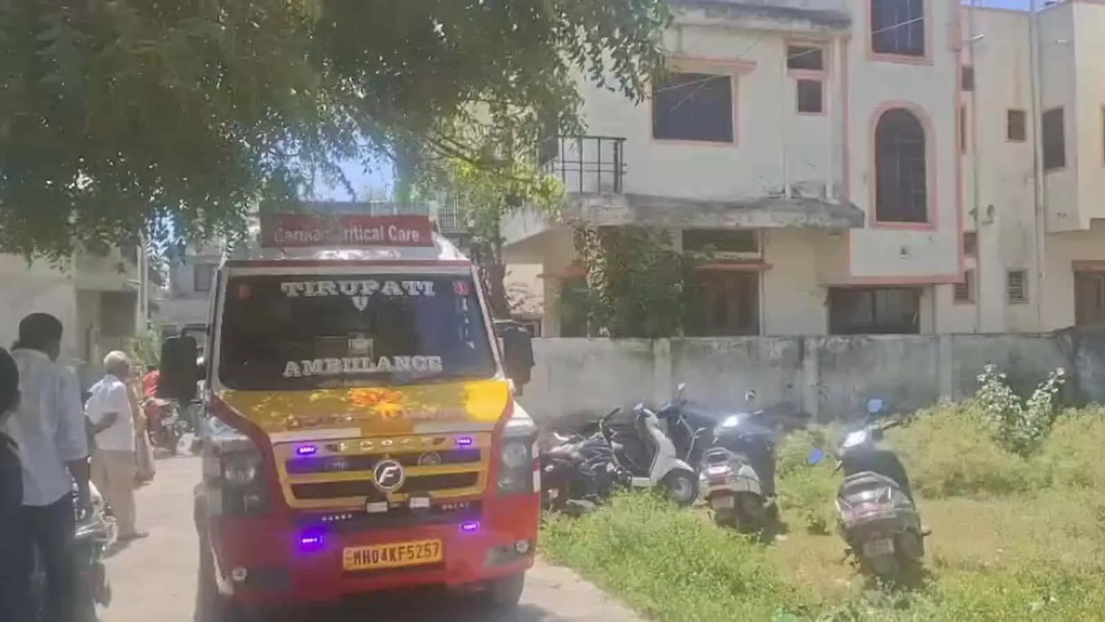 तस्वीर में दिख रही एक इमारत के बाहर एम्बुलेंस खड़ी है और आसपास लोग मौजूद हैं।