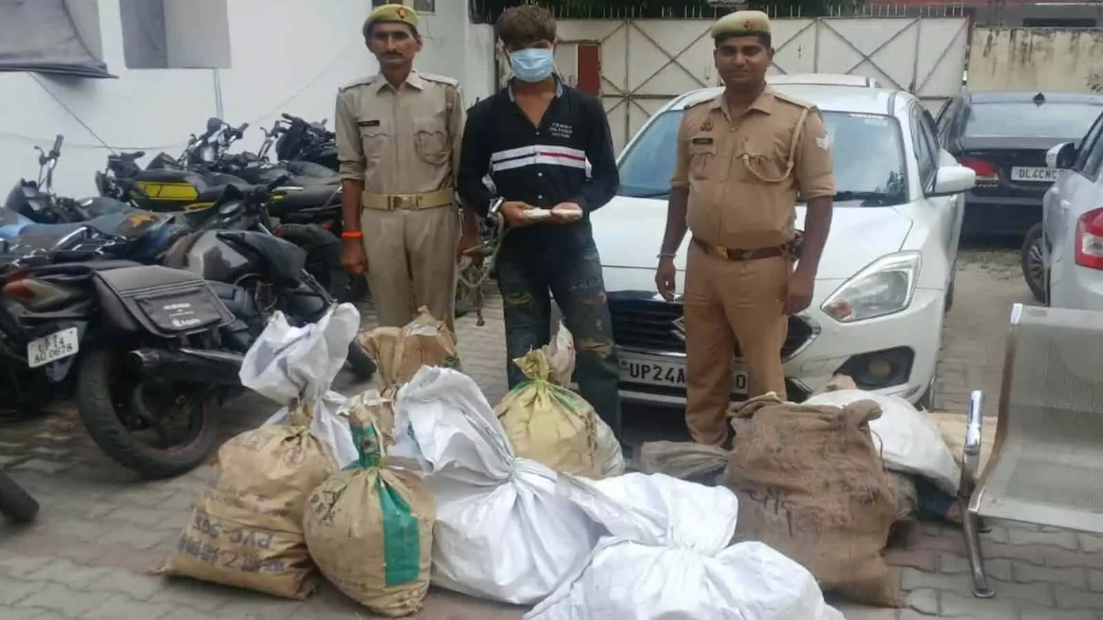 तस्वीर में दो पुलिसकर्मियों के बीच खड़े मास्क पहने आरोपी के आगे जमीन पर चोरी के सामान से भरी बोरियां रखी हैं। तस्वीर में दो पुलिसकर्मियों के बीच खड़े मास्क पहने आरोपी के आगे जमीन पर चोरी के सामान से भरी बोरियां रखी हैं।