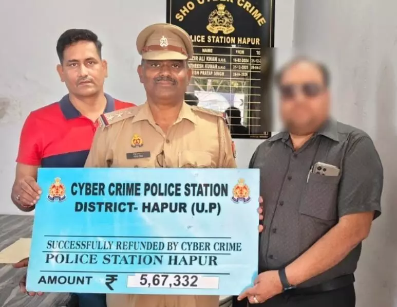 तस्वीर में बाईं तरफ लाल टी-शर्ट पहने व्यक्ति, बीच में पुलिस अधिकारी और दाईं तरफ खड़े व्यक्ति के हाथ में Cyber Crime Police Station District Hapur का बोर्ड है। तस्वीर में बाईं तरफ लाल टी-शर्ट पहने व्यक्ति, बीच में पुलिस अधिकारी और दाईं तरफ खड़े व्यक्ति के हाथ में Cyber Crime Police Station District Hapur का बोर्ड है।