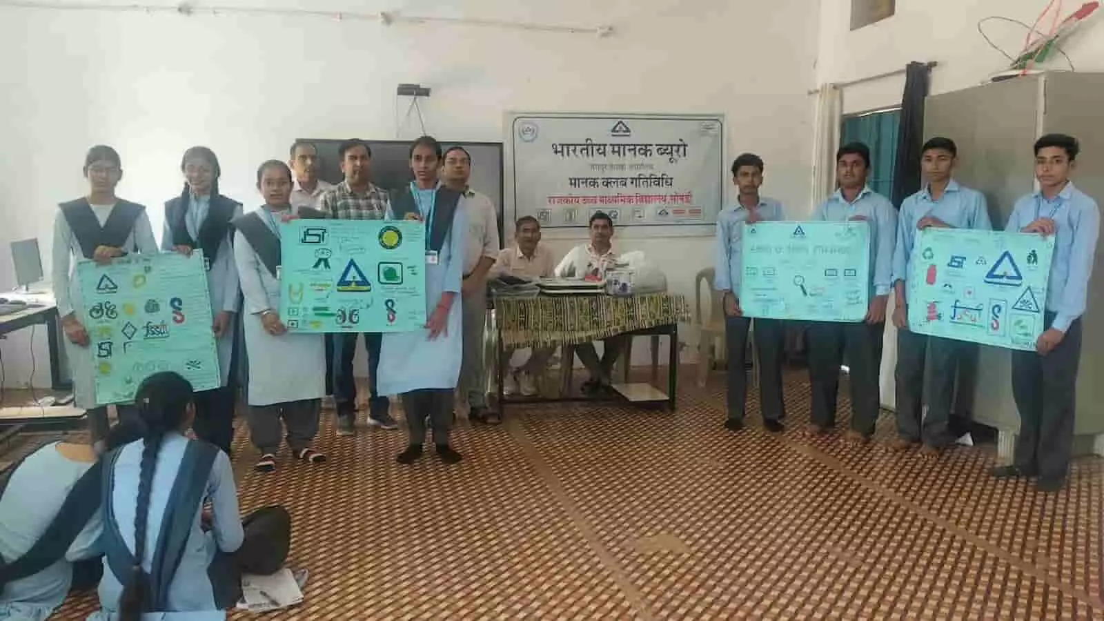 तस्वीर में दिख रही कमरे की पृष्ठभूमि में छात्र और शिक्षक पोस्टर प्रदर्शित करते हुए खड़े हैं। तस्वीर में दिख रही कमरे की पृष्ठभूमि में छात्र और शिक्षक पोस्टर प्रदर्शित करते हुए खड़े हैं।
