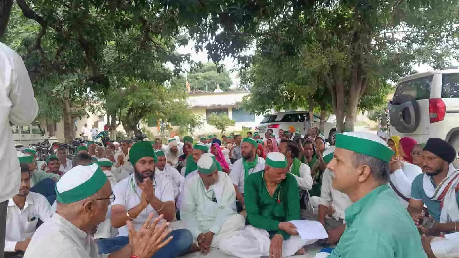 तस्वीर में दिख रही जगह पर हरी टोपी पहने किसान जमीन पर बैठकर चर्चा करते नजर आ रहे हैं। तस्वीर में दिख रही जगह पर हरी टोपी पहने किसान जमीन पर बैठकर चर्चा करते नजर आ रहे हैं।
