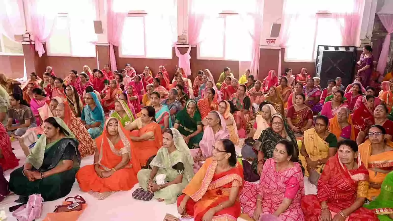 तस्वीर में हॉल के फर्श पर बैठीं कई महिलाएं धार्मिक प्रवचन सुन रही हैं। तस्वीर में हॉल के फर्श पर बैठीं कई महिलाएं धार्मिक प्रवचन सुन रही हैं।