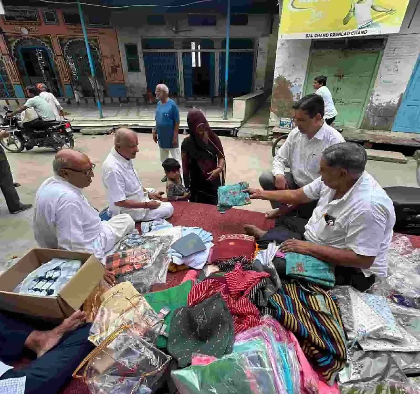 तस्वीर में जमीन पर बैठे लोग सामने खड़ी महिला और बच्चे को कपड़े दे रहे हैं। तस्वीर में जमीन पर बैठे लोग सामने खड़ी महिला और बच्चे को कपड़े दे रहे हैं।