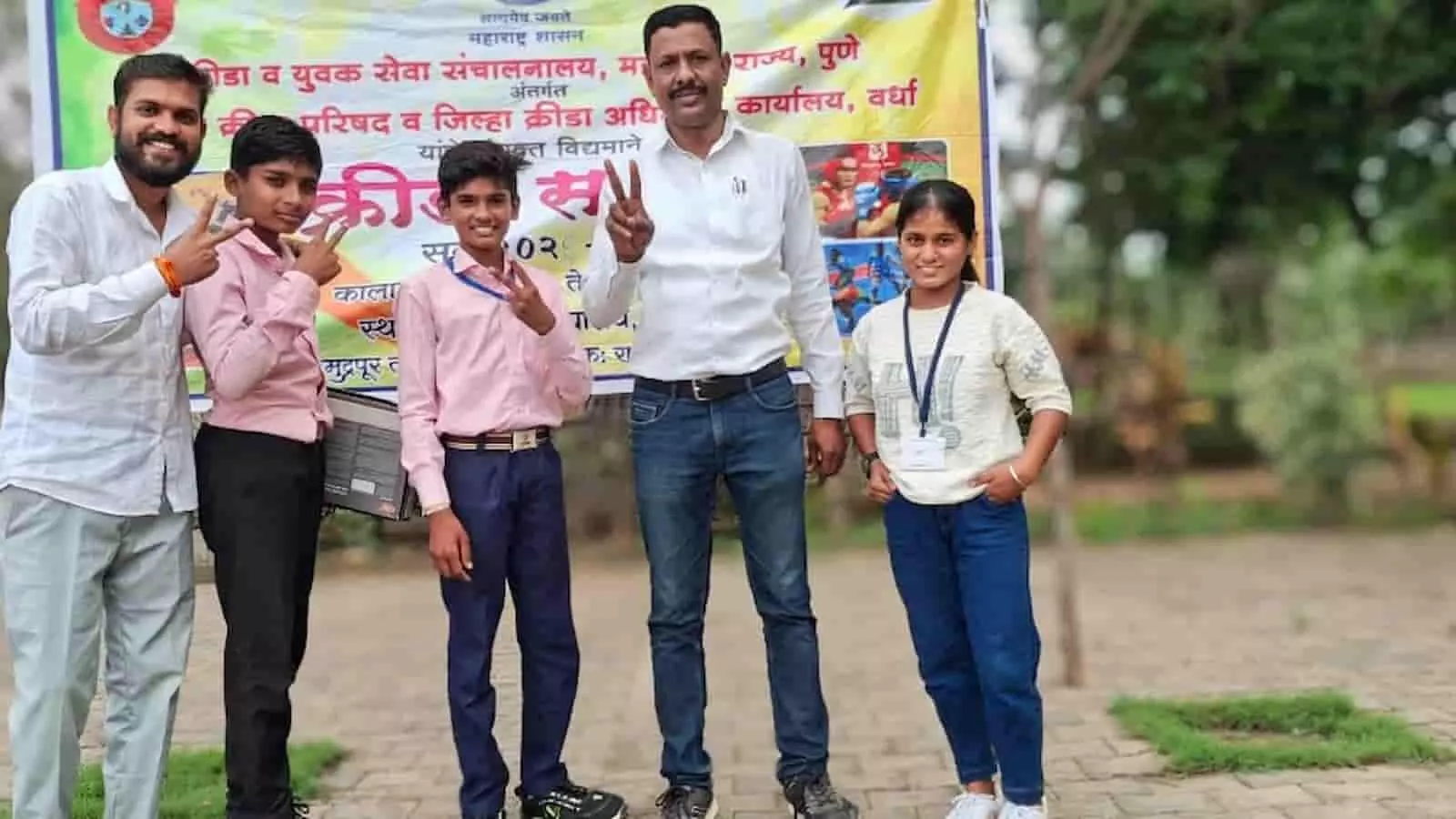 तस्वीर में बाएं से दाएं दो छात्र, शिक्षक और छात्रा विक्ट्री साइन बनाते हुए खड़े हैं। तस्वीर में बाएं से दाएं दो छात्र, शिक्षक और छात्रा विक्ट्री साइन बनाते हुए खड़े हैं।