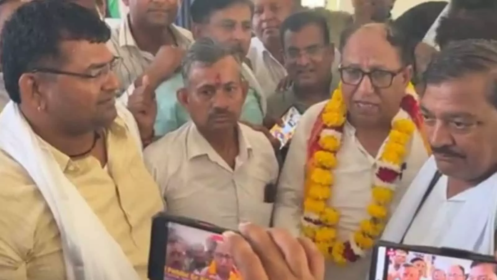 तस्वीर में दिख रही भीड़ के बीच माला पहने व्यक्ति मोबाइल कैमरों के सामने बात करते नजर आ रहे हैं। तस्वीर में दिख रही भीड़ के बीच माला पहने व्यक्ति मोबाइल कैमरों के सामने बात करते नजर आ रहे हैं।