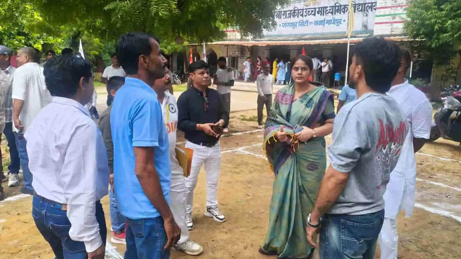 तस्वीर में दिख रही साड़ी पहनी महिला और अन्य लोग विद्यालय परिसर के मैदान में खड़े हैं। तस्वीर में दिख रही साड़ी पहनी महिला और अन्य लोग विद्यालय परिसर के मैदान में खड़े हैं।