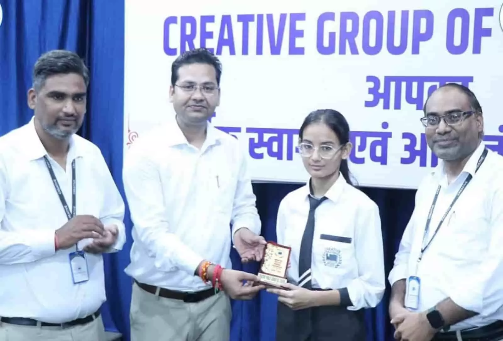 तस्वीर में बाएं से दाएं, तीन शिक्षक और एक छात्रा ट्रॉफी पकड़े हुए खड़े दिखाई दे रहे हैं। तस्वीर में बाएं से दाएं, तीन शिक्षक और एक छात्रा ट्रॉफी पकड़े हुए खड़े दिखाई दे रहे हैं।