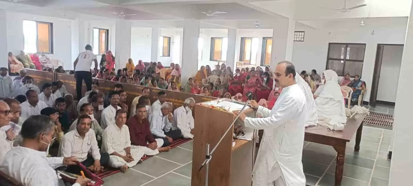 तस्वीर में दांयी ओर पॉडियम पर व्यक्ति माइक के सामने बोल रहा है और सामने हॉल में लोग बैठे हैं। तस्वीर में दांयी ओर पॉडियम पर व्यक्ति माइक के सामने बोल रहा है और सामने हॉल में लोग बैठे हैं।