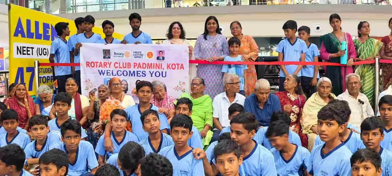 सिनेमाघर परिसर के हॉल में रोटरी क्लब पद्मिनी के बैनर के पीछे खड़े सदस्य, बुजुर्ग और बच्चे। सिनेमाघर परिसर के हॉल में रोटरी क्लब पद्मिनी के बैनर के पीछे खड़े सदस्य, बुजुर्ग और बच्चे।
