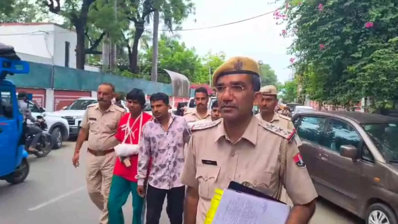 तस्वीर में आगे चल रहे पुलिस अधिकारी के पीछे पुलिसकर्मियों की सुरक्षा में लाल टी-शर्ट और पट्टी बंधे हाथ वाला आरोपी तथा अन्य लोग सड़क पर चलते दिखाई दे रहे हैं। तस्वीर में आगे चल रहे पुलिस अधिकारी के पीछे पुलिसकर्मियों की सुरक्षा में लाल टी-शर्ट और पट्टी बंधे हाथ वाला आरोपी तथा अन्य लोग सड़क पर चलते दिखाई दे रहे हैं।