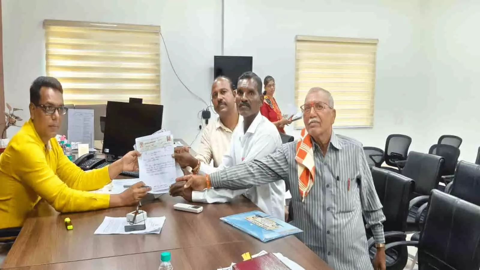 तस्वीर में कार्यालय के कमरे में मेज के पास बैठे हुए कुछ लोग कागजात या आवेदन पत्र थामे हुए दिखाई दे रहे हैं। तस्वीर में कार्यालय के कमरे में मेज के पास बैठे हुए कुछ लोग कागजात या आवेदन पत्र थामे हुए दिखाई दे रहे हैं।