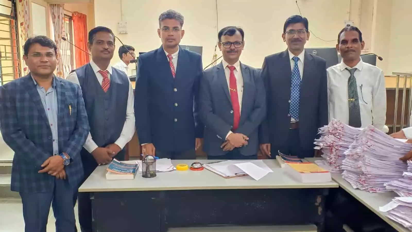 तस्वीर में सूट और टाई पहने हुए अधिकारियों और लोगों का एक समूह मेज के पास खड़े होकर दिखाई दे रहा है. तस्वीर में सूट और टाई पहने हुए अधिकारियों और लोगों का एक समूह मेज के पास खड़े होकर दिखाई दे रहा है.