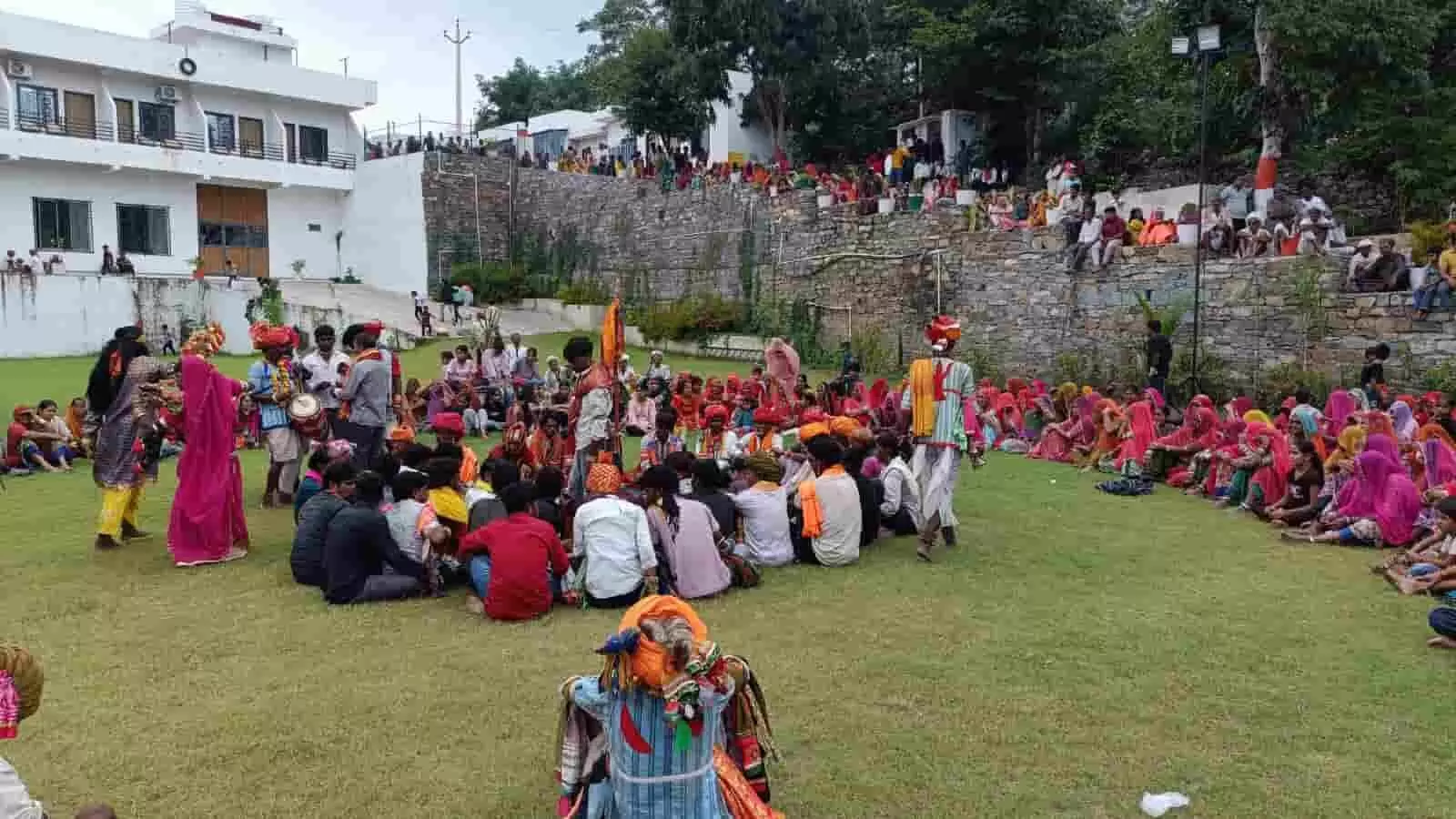 तस्वीर में दिखे मैदान में घेरा बनाकर बैठे ग्रामीणों के बीच पारंपरिक पोशाक पहने कलाकार गवरी नृत्य कर रहे हैं। तस्वीर में दिखे मैदान में घेरा बनाकर बैठे ग्रामीणों के बीच पारंपरिक पोशाक पहने कलाकार गवरी नृत्य कर रहे हैं।