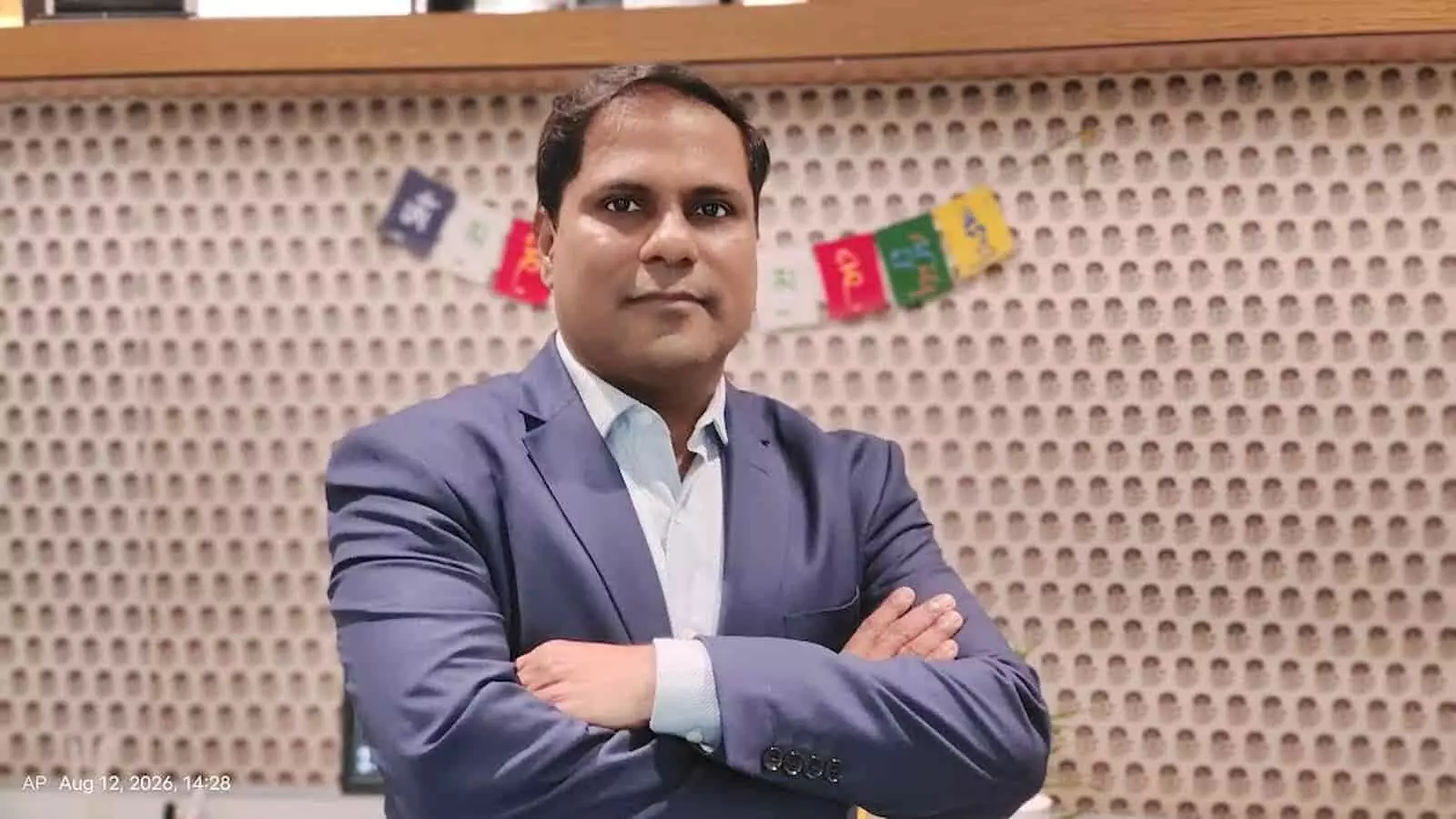 तस्वीर में दिख रही शख्सियत नीले रंग के सूट में हाथ बांधे खड़े होकर मुस्कुरा रही है। तस्वीर में दिख रही शख्सियत नीले रंग के सूट में हाथ बांधे खड़े होकर मुस्कुरा रही है।