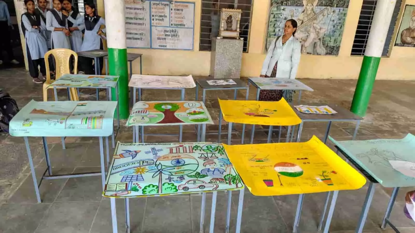 तस्वीर में स्कूल की मेजों पर रखी चित्रकारी प्रतियोगिता की पेंटिंग्स और छात्राएं दिख रही हैं। तस्वीर में स्कूल की मेजों पर रखी चित्रकारी प्रतियोगिता की पेंटिंग्स और छात्राएं दिख रही हैं।
