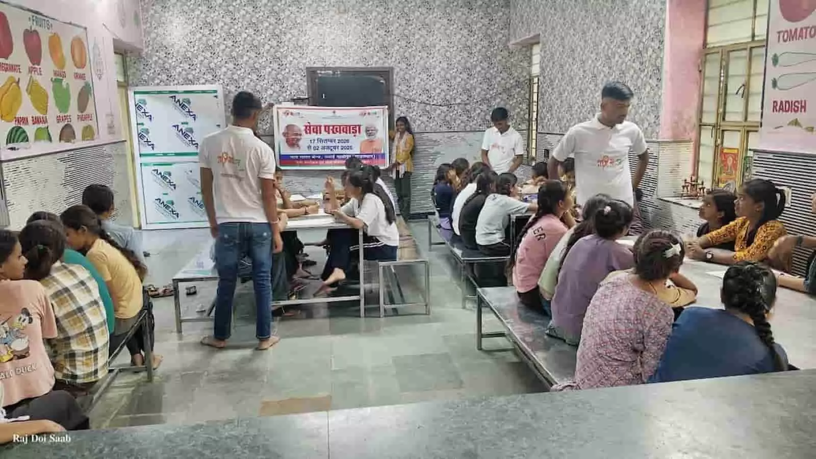तस्वीर में छात्रावास के कमरे में लंबी मेजों पर बैठी छात्राएं चित्रकला प्रतियोगिता में भाग ले रही हैं और उनके पास युवा खड़े हैं। तस्वीर में छात्रावास के कमरे में लंबी मेजों पर बैठी छात्राएं चित्रकला प्रतियोगिता में भाग ले रही हैं और उनके पास युवा खड़े हैं।