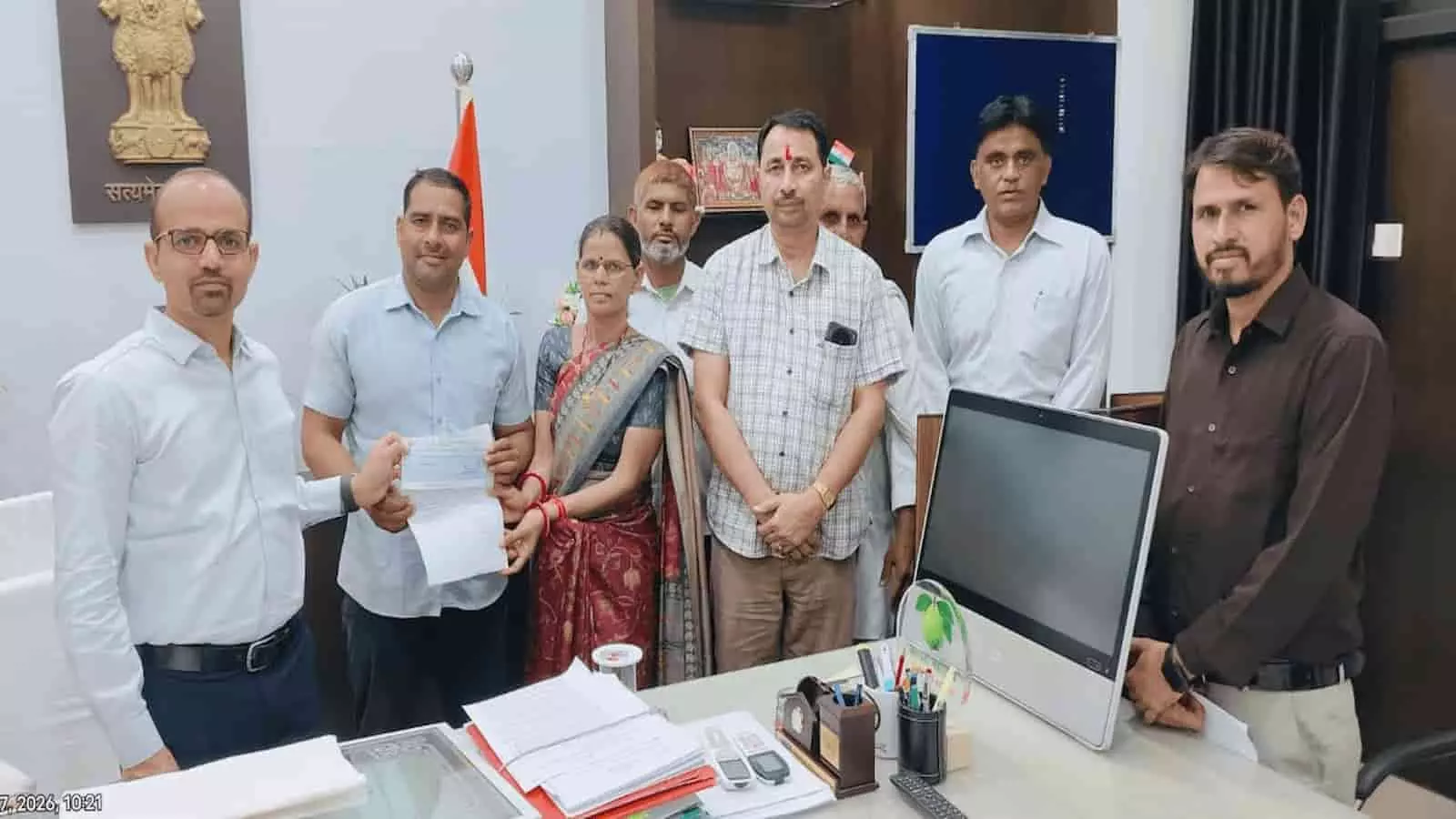 तस्वीर में बाएं से दाएं खड़े कई लोग कार्यालय में एक दूसरे को चेक और दस्तावेज सौंप रहे हैं। तस्वीर में बाएं से दाएं खड़े कई लोग कार्यालय में एक दूसरे को चेक और दस्तावेज सौंप रहे हैं।