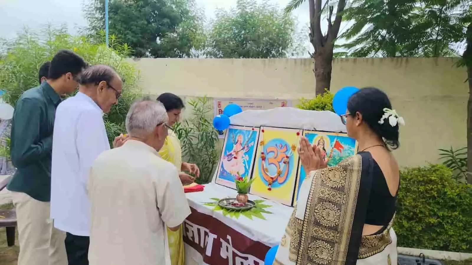 तस्वीर में बाएं से दाएं खड़े कई लोग और सामने दाईं ओर साड़ी पहने महिला हाथ जोड़कर विज्ञान मेले के मंच के सामने खड़ी हैं। तस्वीर में बाएं से दाएं खड़े कई लोग और सामने दाईं ओर साड़ी पहने महिला हाथ जोड़कर विज्ञान मेले के मंच के सामने खड़ी हैं।