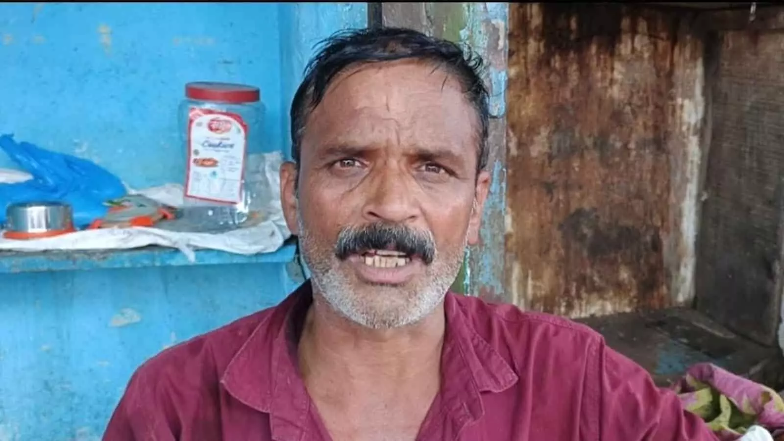 तस्वीर में मूछों वाले एक व्यक्ति लाल रंग की शर्ट पहने हुए नीली दीवार के सामने खड़े होकर कैमरे की तरफ देख रहे हैं। तस्वीर में मूछों वाले एक व्यक्ति लाल रंग की शर्ट पहने हुए नीली दीवार के सामने खड़े होकर कैमरे की तरफ देख रहे हैं।