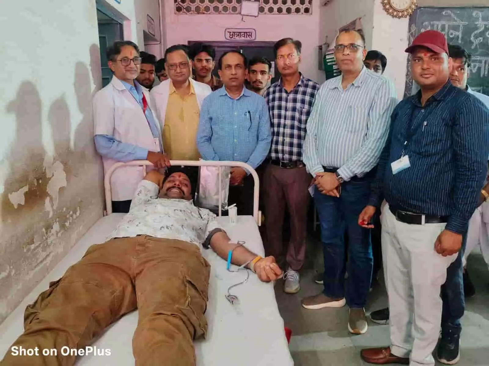 तस्वीर में बाएं से दाएं अस्पताल के बिस्तर पर लेटे हुए एक व्यक्ति को खून देते हुए दिखाया गया है और उनके पास कई लोग खड़े हैं। तस्वीर में बाएं से दाएं अस्पताल के बिस्तर पर लेटे हुए एक व्यक्ति को खून देते हुए दिखाया गया है और उनके पास कई लोग खड़े हैं।