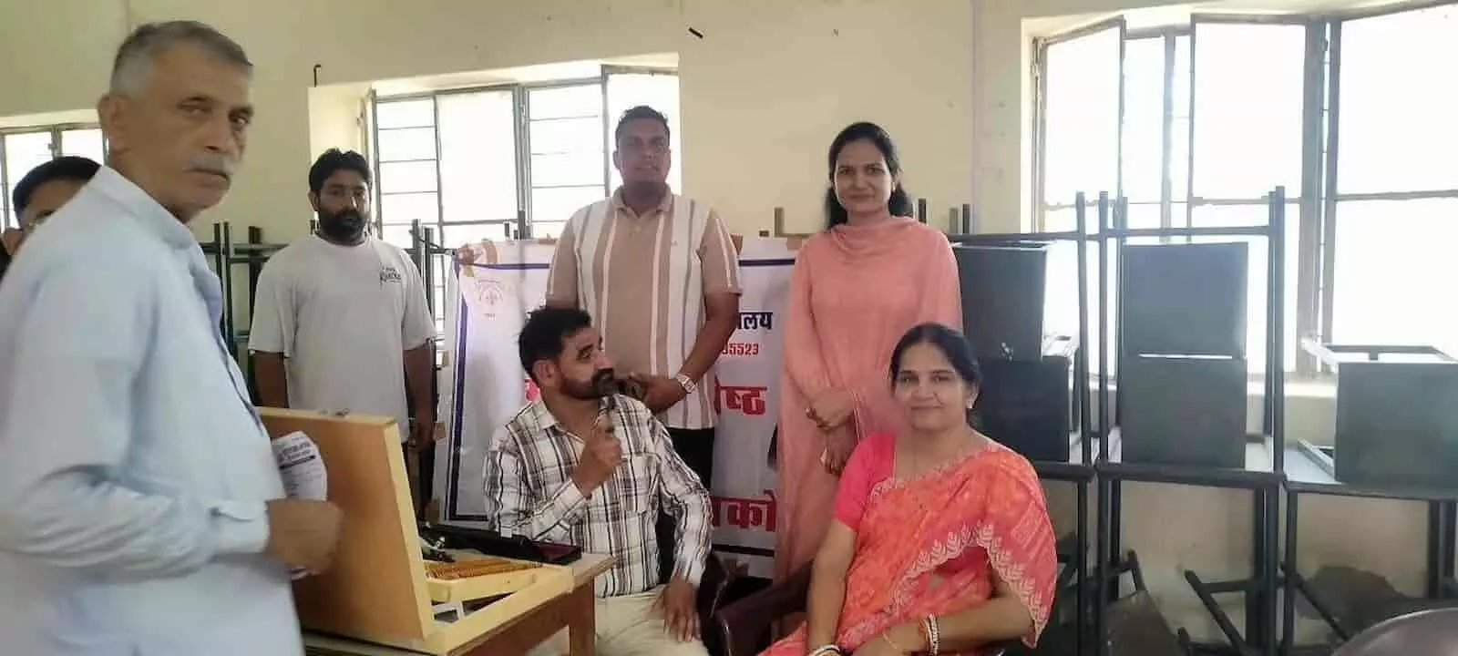 तस्वीर में नोहर कॉलेज कमरे में नेत्र जांच उपकरण के पास खड़े और बैठे लोग visible हैं। तस्वीर में नोहर कॉलेज कमरे में नेत्र जांच उपकरण के पास खड़े और बैठे लोग visible हैं।