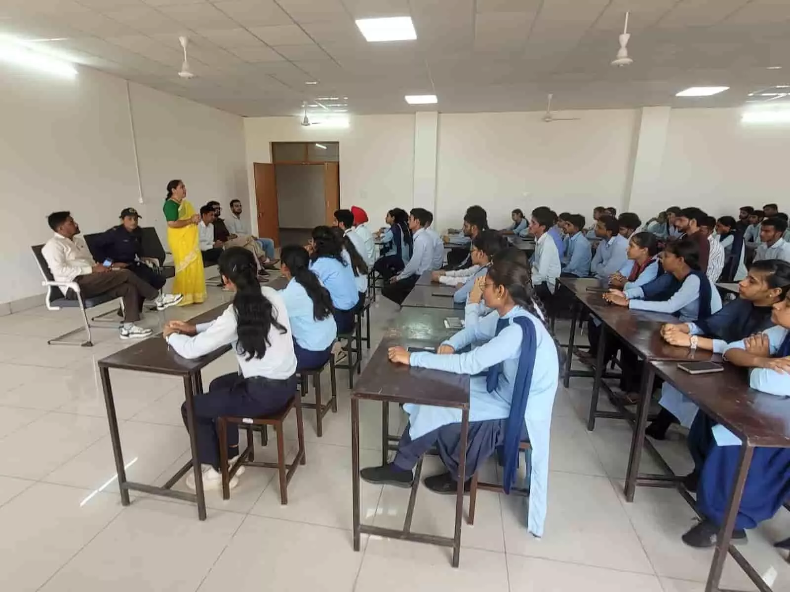 तस्वीर में एक कमरे में बैंचों पर बैठे विद्यार्थियों के सामने पीली साड़ी पहने महिला अधिकारी भाषण दे रही हैं। तस्वीर में एक कमरे में बैंचों पर बैठे विद्यार्थियों के सामने पीली साड़ी पहने महिला अधिकारी भाषण दे रही हैं।