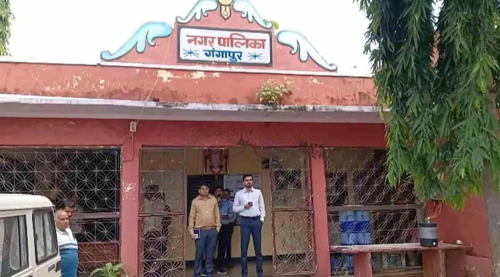 तस्वीर में दिख रही गंगापुर नगरपालिका कार्यालय की इमारत के सामने खड़े लोग और मुख्य बोर्ड। तस्वीर में दिख रही गंगापुर नगरपालिका कार्यालय की इमारत के सामने खड़े लोग और मुख्य बोर्ड।