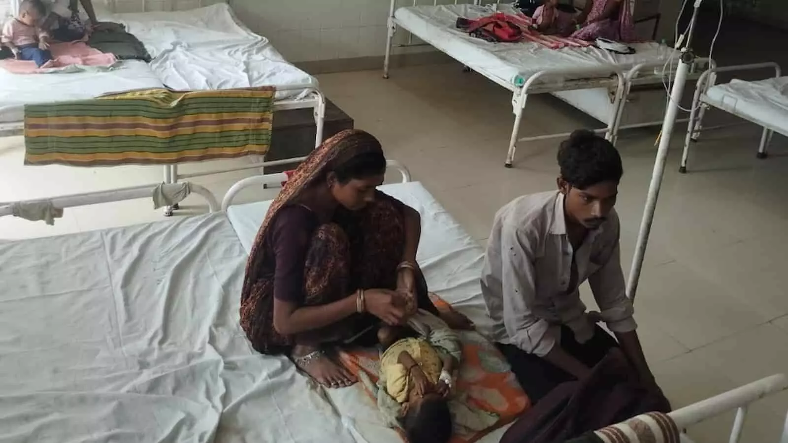 अस्पताल के वार्ड में बेड पर बैठे परिजन और लेटा हुआ बच्चा। अस्पताल के वार्ड में बेड पर बैठे परिजन और लेटा हुआ बच्चा।