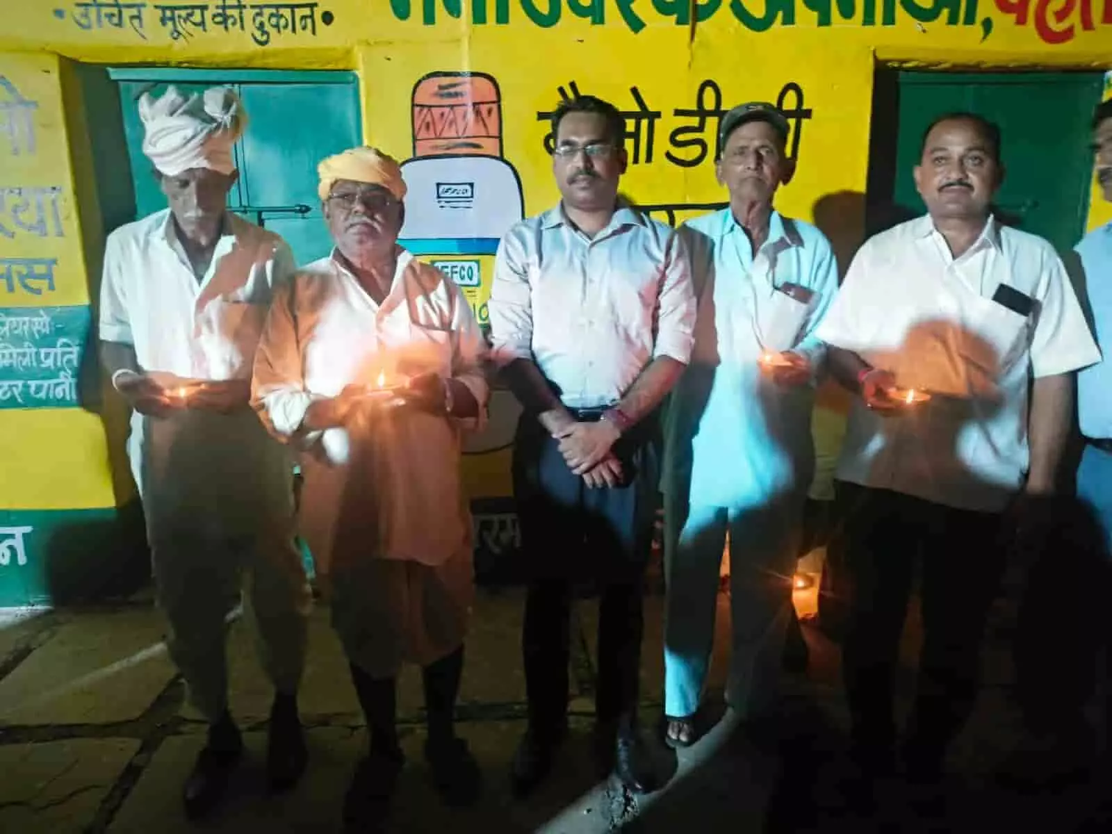 तस्वीर में दिख रही एक इमारत के सामने बाईं से दाईं ओर खड़े लोग हाथ में दीया प्रज्वलित किए हुए हैं। तस्वीर में दिख रही एक इमारत के सामने बाईं से दाईं ओर खड़े लोग हाथ में दीया प्रज्वलित किए हुए हैं।