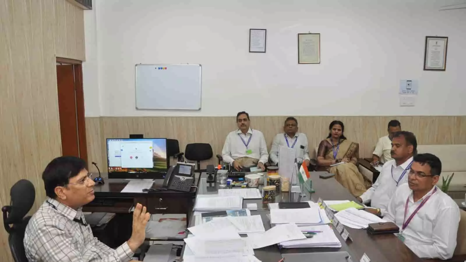 तस्वीर में दिख रही बैठक में एक अधिकारी मेज पर बैठकर अन्य अधिकारियों से चर्चा कर रहे हैं। तस्वीर में दिख रही बैठक में एक अधिकारी मेज पर बैठकर अन्य अधिकारियों से चर्चा कर रहे हैं।