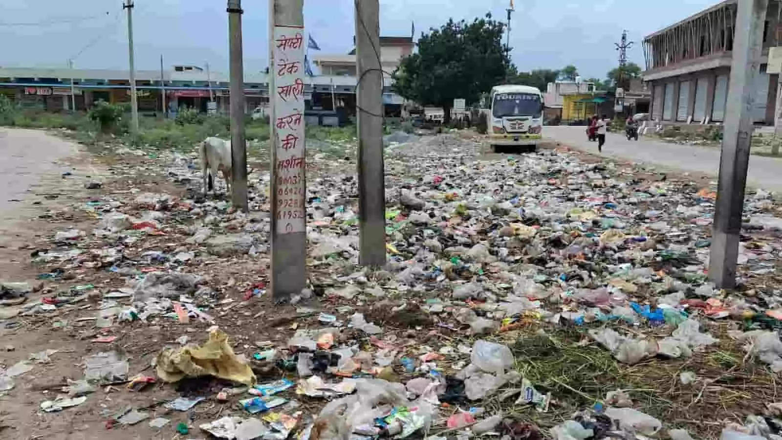 तस्वीर में दिख रही सड़क के किनारे कचरा बिखरा है और पृष्ठभूमि में बस खड़ी है। तस्वीर में दिख रही सड़क के किनारे कचरा बिखरा है और पृष्ठभूमि में बस खड़ी है।