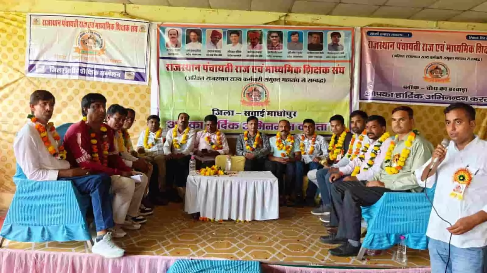 तस्वीर में दिख रही शिक्षक सम्मेलन की सभा में एक व्यक्ति माइक पर बोल रहा है। तस्वीर में दिख रही शिक्षक सम्मेलन की सभा में एक व्यक्ति माइक पर बोल रहा है।