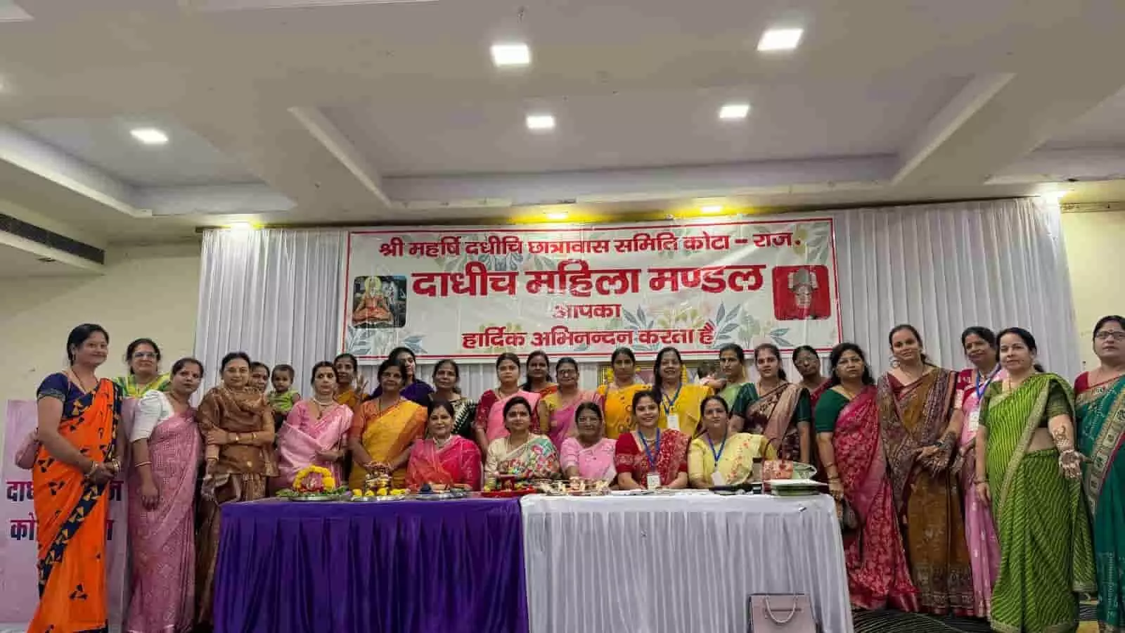 तस्वीर में दाधीच समाज की महिलाएं एक हॉल में बैनर और मंच के पीछे खड़ी हैं। तस्वीर में दाधीच समाज की महिलाएं एक हॉल में बैनर और मंच के पीछे खड़ी हैं।