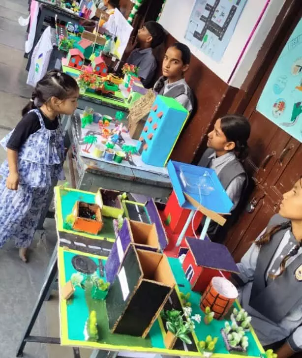 तस्वीर में स्कूल के बरामदे में रखी मेजों पर विद्यार्थी विज्ञान और गणित के मॉडल प्रदर्शित कर रहे हैं। तस्वीर में स्कूल के बरामदे में रखी मेजों पर विद्यार्थी विज्ञान और गणित के मॉडल प्रदर्शित कर रहे हैं।