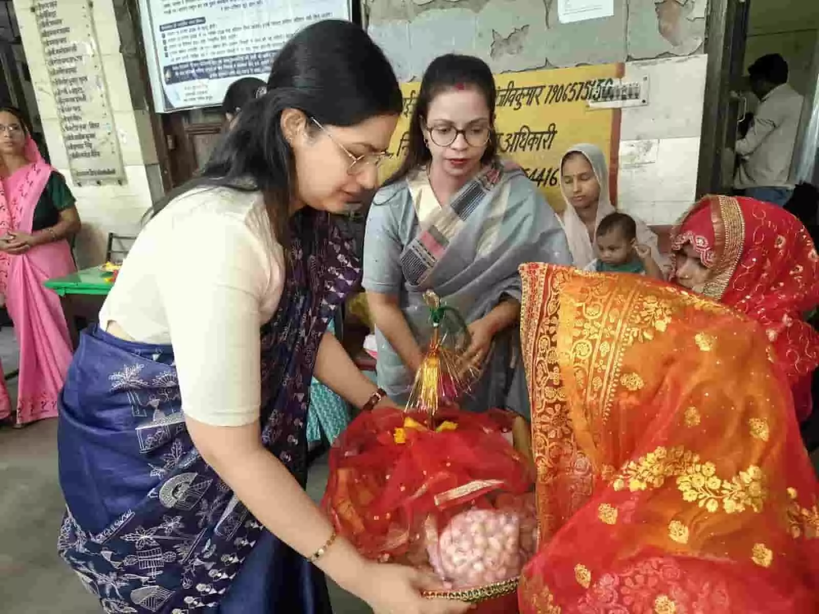 तस्वीर में दिख रही महिला अधिकारी बाईं ओर खड़ी होकर महिला को टोकरी में रखी सामग्री दे रही हैं। तस्वीर में दिख रही महिला अधिकारी बाईं ओर खड़ी होकर महिला को टोकरी में रखी सामग्री दे रही हैं।