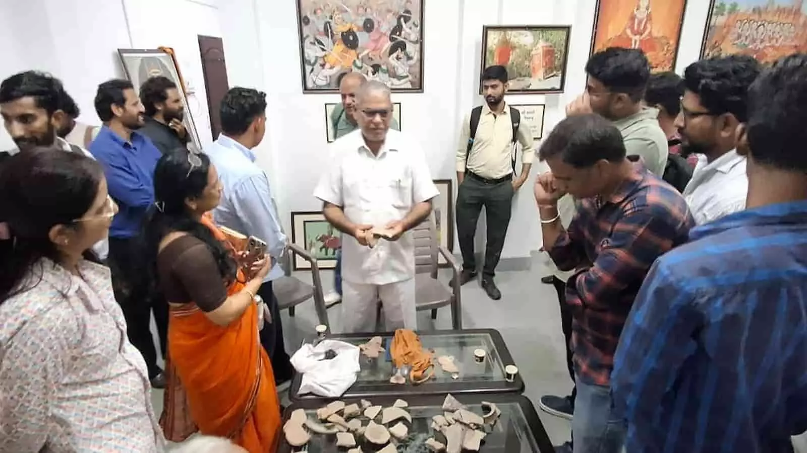 तस्वीर में एक व्यक्ति केंद्र में खड़े होकर कुछ वस्तुएं दिखा रहा है और चारों तरफ लोग खड़े होकर उन्हें देख रहे हैं। तस्वीर में एक व्यक्ति केंद्र में खड़े होकर कुछ वस्तुएं दिखा रहा है और चारों तरफ लोग खड़े होकर उन्हें देख रहे हैं।