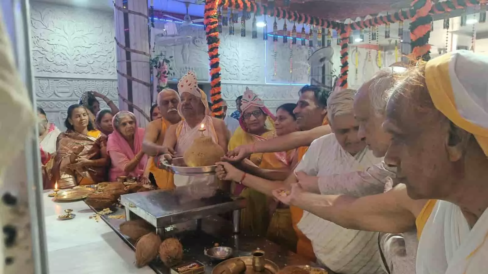 तस्वीर में बाएं से दाएं पारंपरिक और सफेद वस्त्रों में खड़े लोग मंदिर में थाली और पूजा सामग्री पकड़े हुए दिखाई दे रहे हैं। तस्वीर में बाएं से दाएं पारंपरिक और सफेद वस्त्रों में खड़े लोग मंदिर में थाली और पूजा सामग्री पकड़े हुए दिखाई दे रहे हैं।