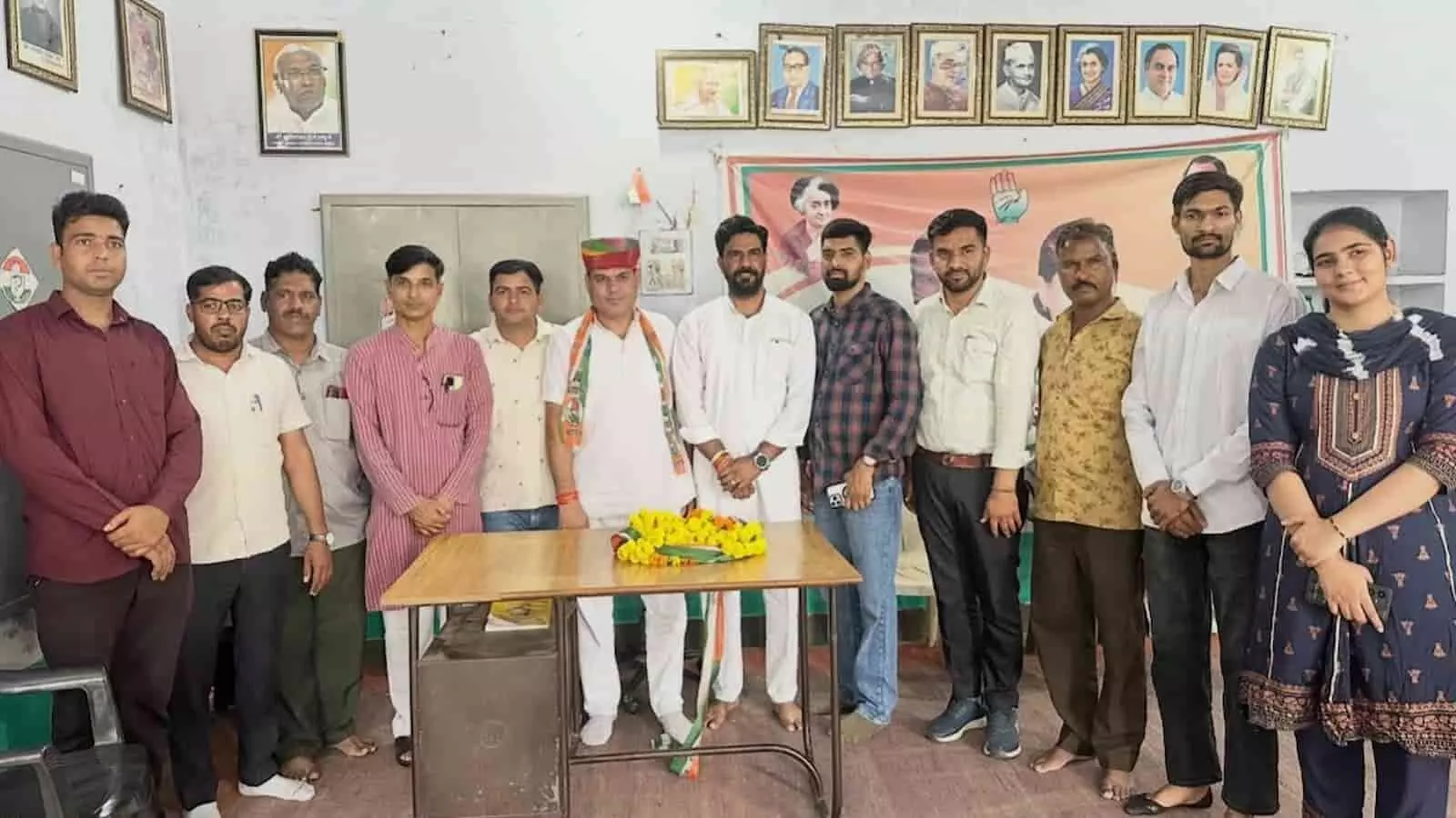 : तस्वीर में बाएं से दाएं विभिन्न कपड़ों में खड़े कई लोग और नेता मेज के पास दिखाई दे रहे हैं। : तस्वीर में बाएं से दाएं विभिन्न कपड़ों में खड़े कई लोग और नेता मेज के पास दिखाई दे रहे हैं।