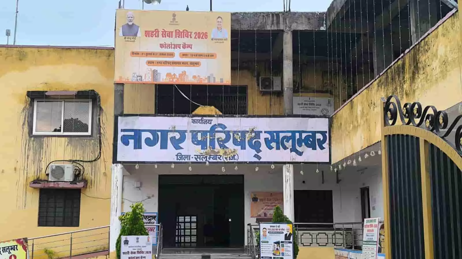 तस्वीर में सामने की ओर सीढ़ियों वाला नगर परिषद का पीला भवन और उस पर लगे बैनर दिखाई दे रहे हैं। तस्वीर में सामने की ओर सीढ़ियों वाला नगर परिषद का पीला भवन और उस पर लगे बैनर दिखाई दे रहे हैं।